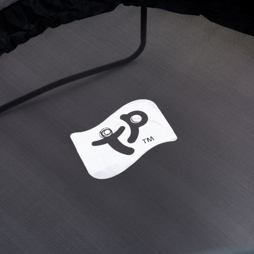Close-up of a gray TP Genius® 12ft Round Trampoline mat with a white rectangular logo featuring stylized black text and a trademark symbol in the center, made by TP Toys and supported by a sturdy galvanized steel frame.