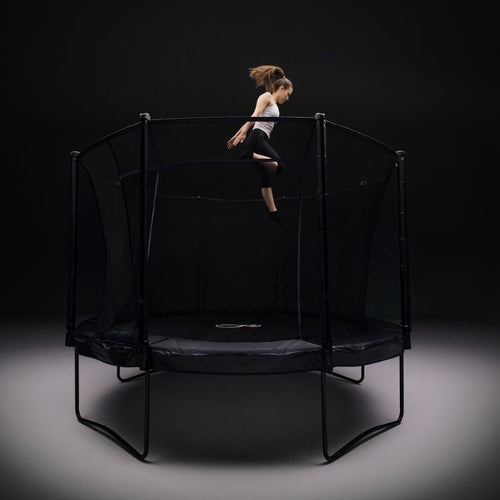 A girl jumps high on the TP Toys 10ft Infinity Round Trampoline with a safety net, set against a dark background, highlighting its superior bounce performance and advanced safety features for worry-free fun.