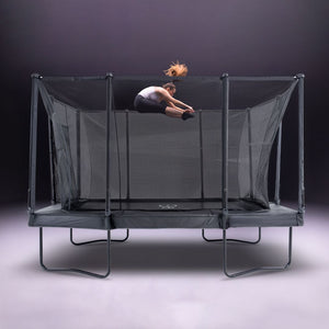 A person does a tuck jump high above the TP Toys Infinity 10ft x 14ft Rectangular Trampoline with net enclosure, set against a neutral background. Easy assembly adds convenience.