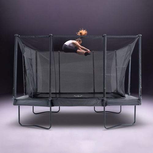 A person does a tuck jump high above the TP Toys Infinity 10ft x 14ft Rectangular Trampoline with net enclosure, set against a neutral background. Easy assembly adds convenience.