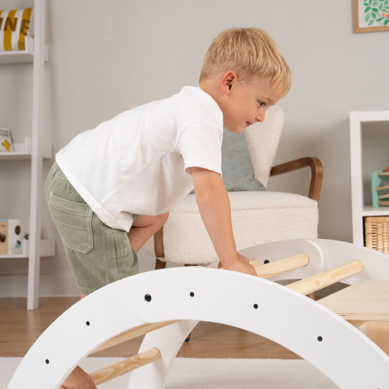 A young boy in a white shirt and green shorts climbs the TP Toys TP Active-Tots Pikler Style Three in One Playset—FSC® certified—exploring the Montessori-inspired climbing set with curiosity and joy in a bright, modern room.