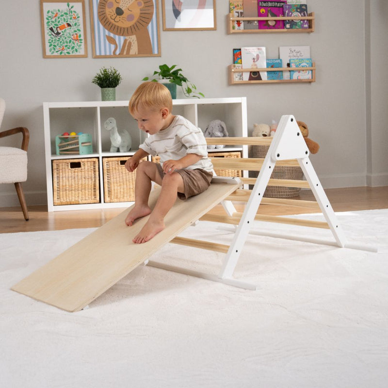 A young child sits atop a TP Toys TP Active-Tots Pikler Style Three in One Playset—FSC® certified—featuring a wooden slide, in a tidy, well-decorated playroom.