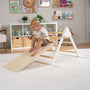 A young child sits atop a TP Toys TP Active-Tots Pikler Style Three in One Playset—FSC® certified—featuring a wooden slide, in a tidy, well-decorated playroom.