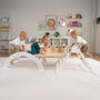 Three young children climb and play on the TP Toys TP Active-Tots Pikler Style Three in One Playset (FSC® certified) in a brightly lit, neatly decorated room with shelves and wall art.