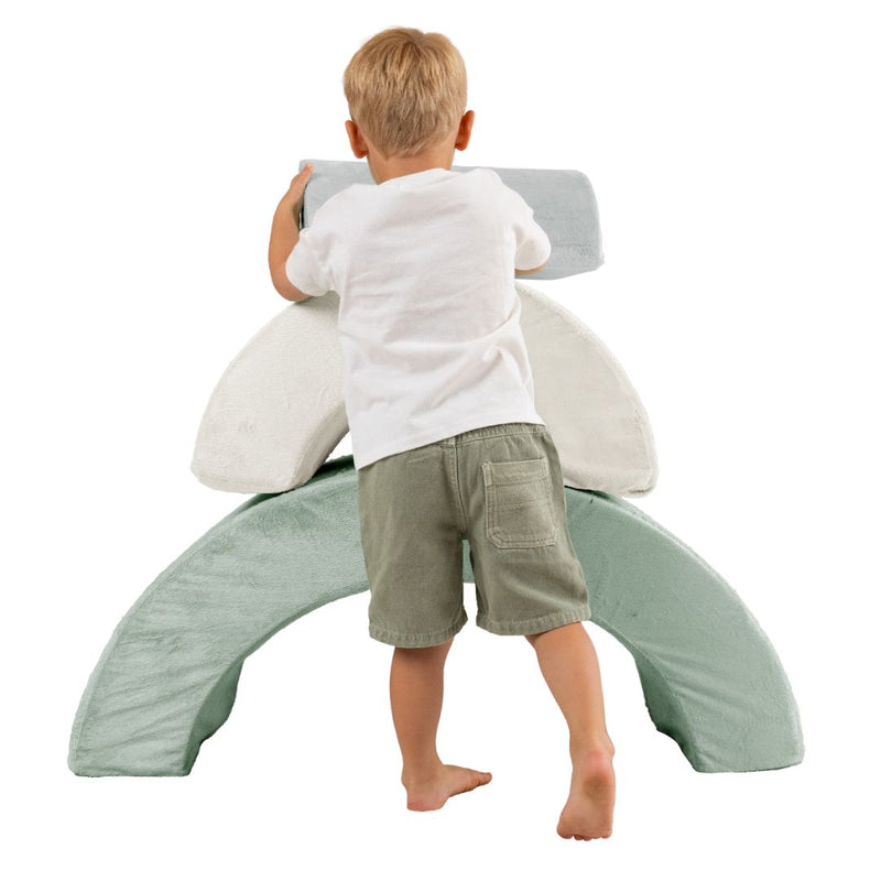 A young child stacks the TP Toys TP Active-Tots Pikler Style Rainbow Arch Playset, building gross motor skills, viewed from behind against a white background.
