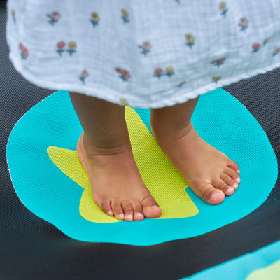 A child in a floral white dress stands barefoot on the Bluey Junior 3ft Trampoline by TP Toys—ready for indoor or outdoor play and perfect for their first bouncing experience.