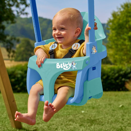 A smiling baby in a yellow outfit enjoys a sunny day outdoors on the TP Toys Bluey Quadpod® 4 in 1 Baby Swing Seat—a versatile swing built for comfort and fun.