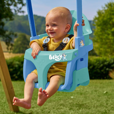 A smiling baby in yellow enjoys the safety of the TP Sherwood Single Wooden Swing Set with Bluey Quadpod by TP Toys, sitting outdoors amid grass and trees on this PEFC-certified swing seat.