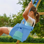 A young child sits in the TP Toys Bluey Quadpod® 4 in 1 Baby Swing Seat, holding the ropes on a wooden playset outdoors, featuring a Bluey cartoon sticker.