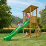 Four children play outdoors on the TP Toys Skywood Wooden Lookout Tower with a 3m super wavy slide, climbing frames, and sandbox in a grassy area on a sunny day. The playset is FSC® certified for sustainable wood.