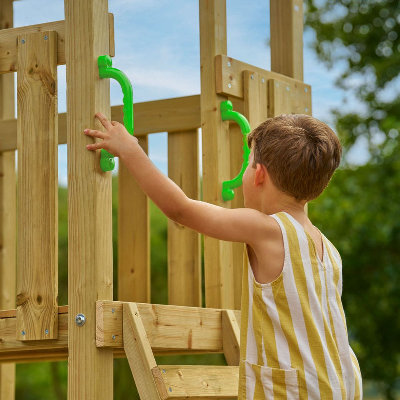 A young child in a yellow and white striped outfit holds green handles while climbing the TP Toys Skywood Wooden Lookout Tower with 3m Super Wavy Slide—an FSC® certified outdoor playset.