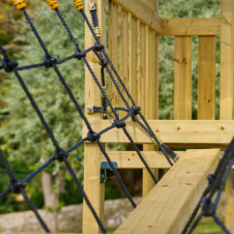 Close-up of the TP Toys Skywood Wooden SkyWalk Bridge, crafted from FSC® certified wood with a black rope climbing net and railings; blurred trees appear in the background.