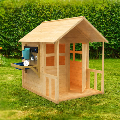 The TP Toys Buttercup Cottage Wooden Playhouse with Floor, Verandah, and Mud Kitchen—FSC® certified—features an open doorway and window. It sits on grass with a hedge behind, offering outdoor fun for kids.
