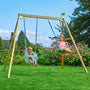 A baby and a young girl are sitting on swings attached to the TP Toys TP Forest Wooden Double Swing Bluey with Quadpod and Rapide Seats – FSC® certified, in a grassy garden with flowers and trees in the background.
