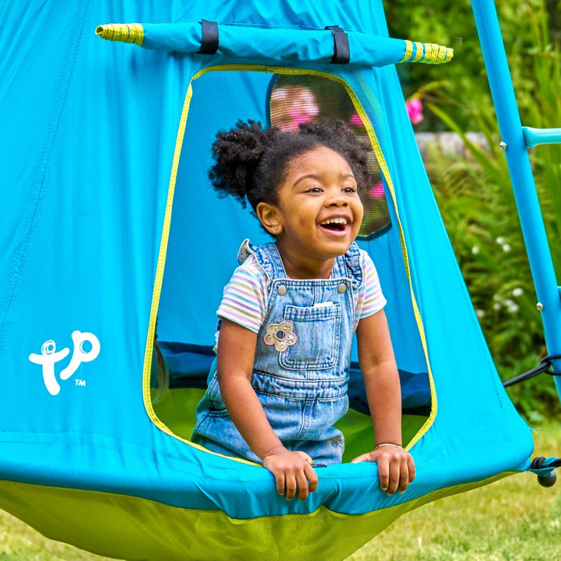 A young child in overalls smiles as they lean out of the TP Toys TP UFO Den & Climbing Frame Blue Edition, enjoying imaginative outdoor play on the grassy lawn.