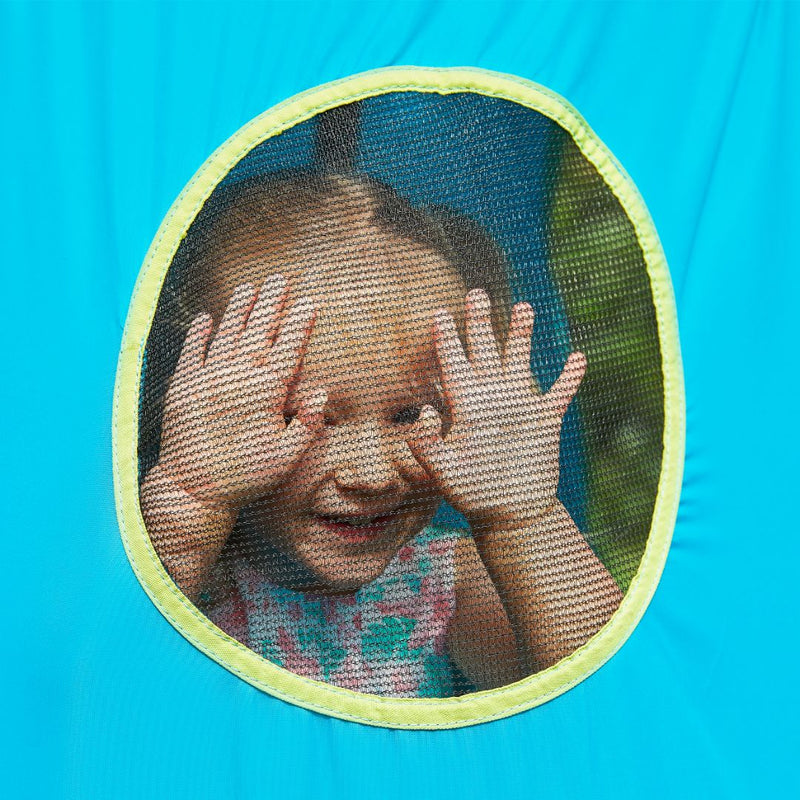 A young child with pigtails smiles playfully, pressing their hands and face against the mesh window of the bright blue TP UFO Den & Climbing Frame Blue Edition by TP Toys—capturing the magic of outdoor play and imagination.