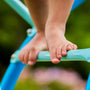 Close-up of a child's bare feet on the blue TP UFO Den & Climbing Frame by TP Toys, set outdoors with a green background—ideal for inspiring imaginative play.
