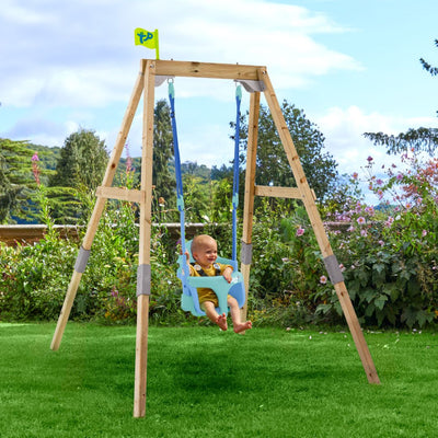 A baby enjoys the TP Toys TP Forest Acorn Growable Swing Set with Bluey Quadpod, FSC® certified, on a wooden frame in a garden with green grass, flowers, and a small yellow flag in the background.