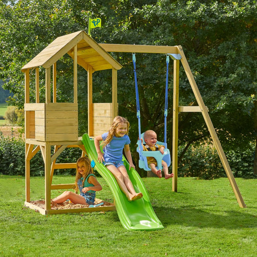 Three kids play in a lush garden on the TP Toys TP Treehouse Wooden Play Tower with Wavy Slide & Bluey Quadpod—one zips down the green slide, another digs in the sandbox, while a baby swings safely. FSC® certified wood blends with nature.
