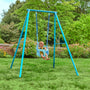 A baby sits in a blue TP Toys Bluey Quadpod on the TP Deluxe Single Metal Swing Set, suspended from its metal frame in a grassy garden with trees and flowers in the background.