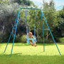 A baby sits in the TP Toys TP Small to Tall 2 in 1 Metal Swing Set with Bluey Quadpod on a grassy lawn, surrounded by trees and bushes on a sunny day.
