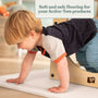 A young child crawls on TP Toys' TP Active-Tots Safety Play Mats beside a wooden play structure, with a sign reading: Soft, non-toxic flooring for your Active-Tots products—ideal for any toddler play area.