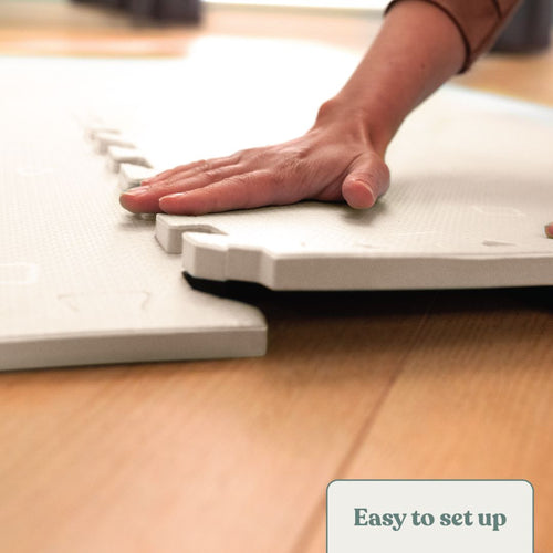 Someone presses down on TP Toys TP Active-Tots Safety Play Mats over a wooden floor, setting up a safe play area for toddlers. A label in the corner reads "Easy to set up.