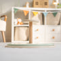 The TP Toys Active-Tots Pikler Style Wooden Spinning Seat—crafted from FSC® certified wood—stands on a light-colored floor in a children’s playroom, surrounded by shelves and colorful pennant bunting in the background.