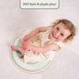 A smiling young child in a cream dress sits on the TP Active-Tots Pikler Style Wooden Spinning Seat by TP Toys—an FSC® certified Montessori toddler toy—on a white carpet, looking up at the camera.