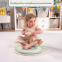 A young child sits cross-legged on the TP Toys TP Active-Tots Pikler Style Wooden Spinning Seat—crafted from FSC® certified wood—in a playroom, holding its handle and engaging in sensory play, with shelves and toys in the background.