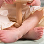 A child dressed in a cream-colored outfit sits cross-legged on the floor, holding the TP Active-Tots Pikler Style Wooden Spinning Seat by TP Toys—an FSC® certified Montessori toddler toy—perfect for sensory play.