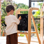 A child draws with yellow chalk on the blackboard of a TP Active-Tots Pikler Style Wooden Helper Tower.