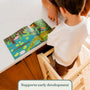 A child stands on a TP Active-Tots Pikler Style Wooden Helper Tower at a counter, reading a picture book with an adult.