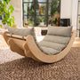 The TP Toys Active-Tots Sway Wooden Rocker with Cushion—crafted from FSC® certified wood—sits atop a textured rug in a sunlit living room, surrounded by large windows and indoor plants, making it an ideal Montessori-inspired toddler rocker that combines style and comfort.