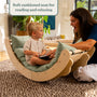 A young child sits on the TP Toys TP Active-Tots Sway Wooden Rocker with Cushion (FSC® certified), reading a book, while an adult woman smiles at him. Text above reads, Soft cushioned seat for reading and relaxing.