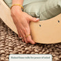 A hand grips the raised wooden base rail of the TP Active-Tots Sway Wooden Rocker with Cushion by TP Toys, shown here in a light finish with a green cushion on top and a woven rug underneath. Text reads: Raised base rails for peace of mind—designed with inspiration from the gentle curves of a Montessori rocker. FSC® certified.