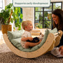 A young child sits in the TP Toys Active-Tots Sway Wooden Rocker with Cushion (FSC® certified), holding a book and smiling at an adult woman. Text above reads, Supports early development. They are in a bright, cozy room.