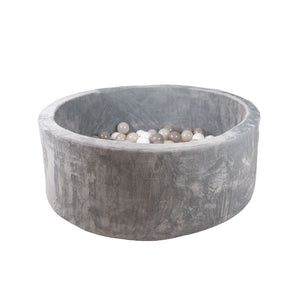 The TP Toys Active Tots Foam Ball Pit with 100 playballs features a round, gray velvet-covered design filled with white, gray, and beige balls, creating an inviting sensory play space against a plain white background.
