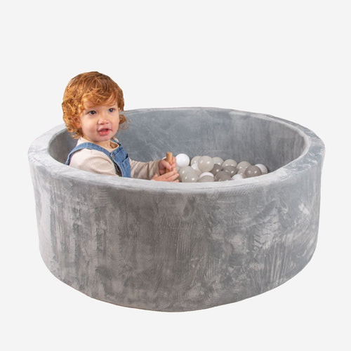 A toddler sits inside a gray TP Toys Active Tots Foam Ball Pit with 100 white and gray playballs for sensory play.