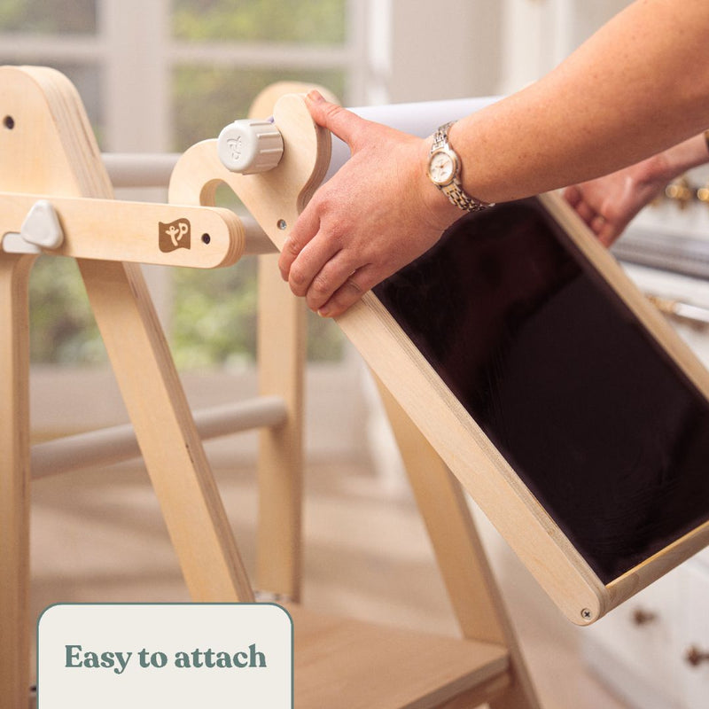 In a bright room, a child attaches the TP Toys TP Active-Tots Pikler Style Wooden Easel Play Accessory (FSC® certified) to a light wooden easel. The “Easy to attach” label makes it an ideal addition to any kid’s creative space.
