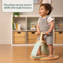 A young child stands on the TP Active-Tots Pikler Style Toddler Bouncer by TP Toys, gripping handlebars, with a text overlay: Develops gross motor skills through bounce. FSC® certified.