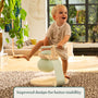 A toddler in a striped romper sits on the TP Active-Tots Pikler Style Toddler Bouncer - FSC® certified by TP Toys, featuring mint green accents, in a bright, modern living room. Text reads: Improved design for better stability.