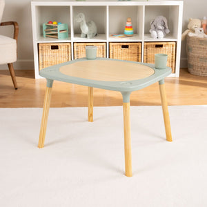 The TP Toys Active-Tots Pikler Style 4 in 1 Wooden Play Table, FSC® certified, is a compact mint green Montessori activity table with two built-in cups, shown on a white rug in a playroom with shelves and baskets behind.