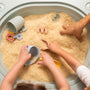 Children and an adult explore dry rice in a sensory bin on the TP Active-Tots Pikler Style 4 in 1 Wooden Play Table by TP Toys, using plastic scoops, cups, and alphabet cutters.