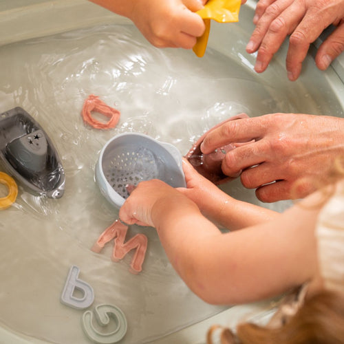 Children and adults play with floating alphabet letters and a toy boat in the TP Toys TP Active-Tots Pikler Style 4 in 1 Wooden Play Table, FSC® certified, filled with water for sensory fun.