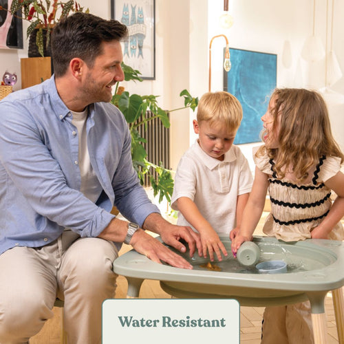 An adult and two children play with water indoors on the TP Active-Tots Pikler Style 4 in 1 Wooden Play Table by TP Toys. The text "Water Resistant" appears at the bottom of the image.