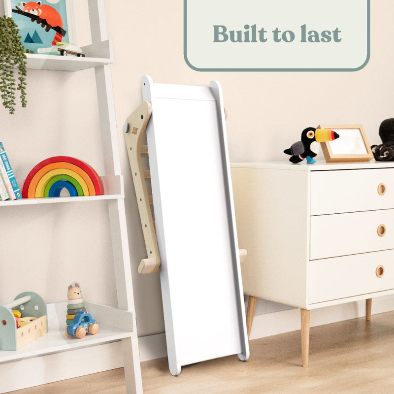 The TP Toys Active-Tots Pikler Style Folding Wooden Slide (FSC® certified) stands beside a white dresser and ladder shelf in a kids’ room. Toys and books are neatly arranged. Built to last—perfect for indoor play and Montessori setups.