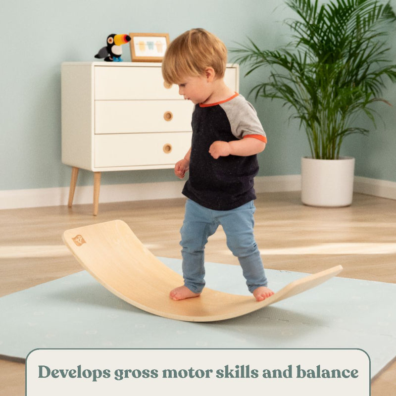 A young child balances on the TP Active-Tots Pikler Style Wooden Balance Board by TP Toys in a playroom. FSC® certified. Text: Boosts gross motor skills and balance with this Montessori-inspired wooden toy.
