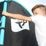 A child holding the blue padded pole of a TP Genius Blue 14ft Round Trampoline enclosure.