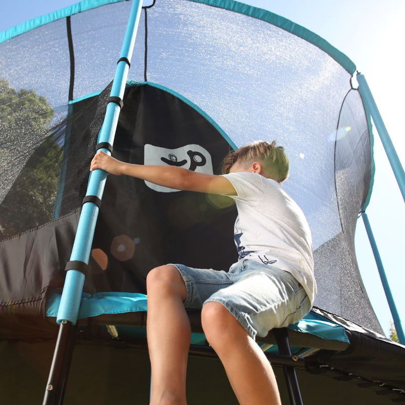 A boy climbing through the zip-free entry of a blue and black TP Genius Blue 14ft Round Trampoline with a SurroundSafe enclosure.